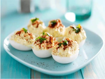 A devilled egg classic on a blue plate and a hard-boiled egg with mayo and toppings of paprika.