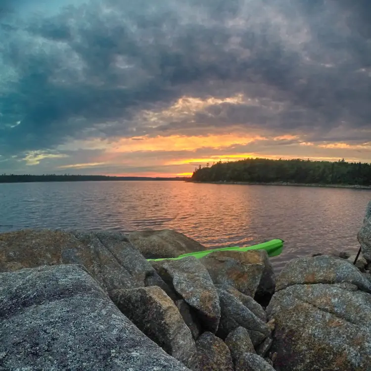 A scene on the lake with stones and kayak with paddle.